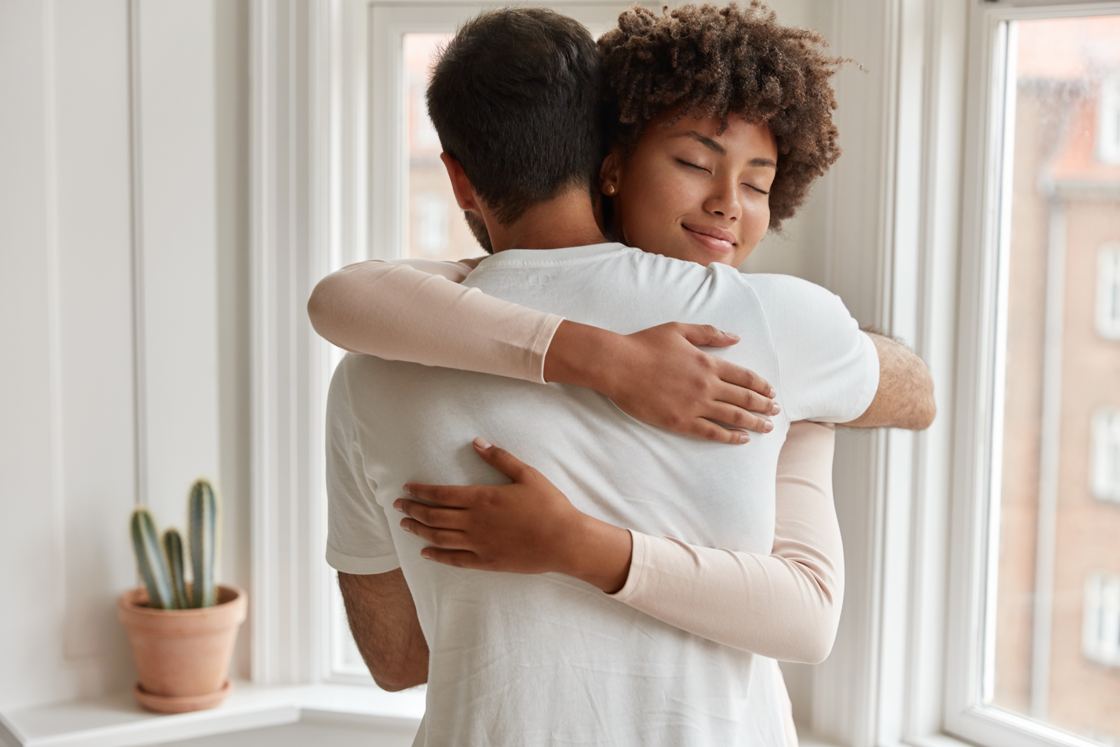 Couple_Embracing_Tenderly_By_Window_Indoors